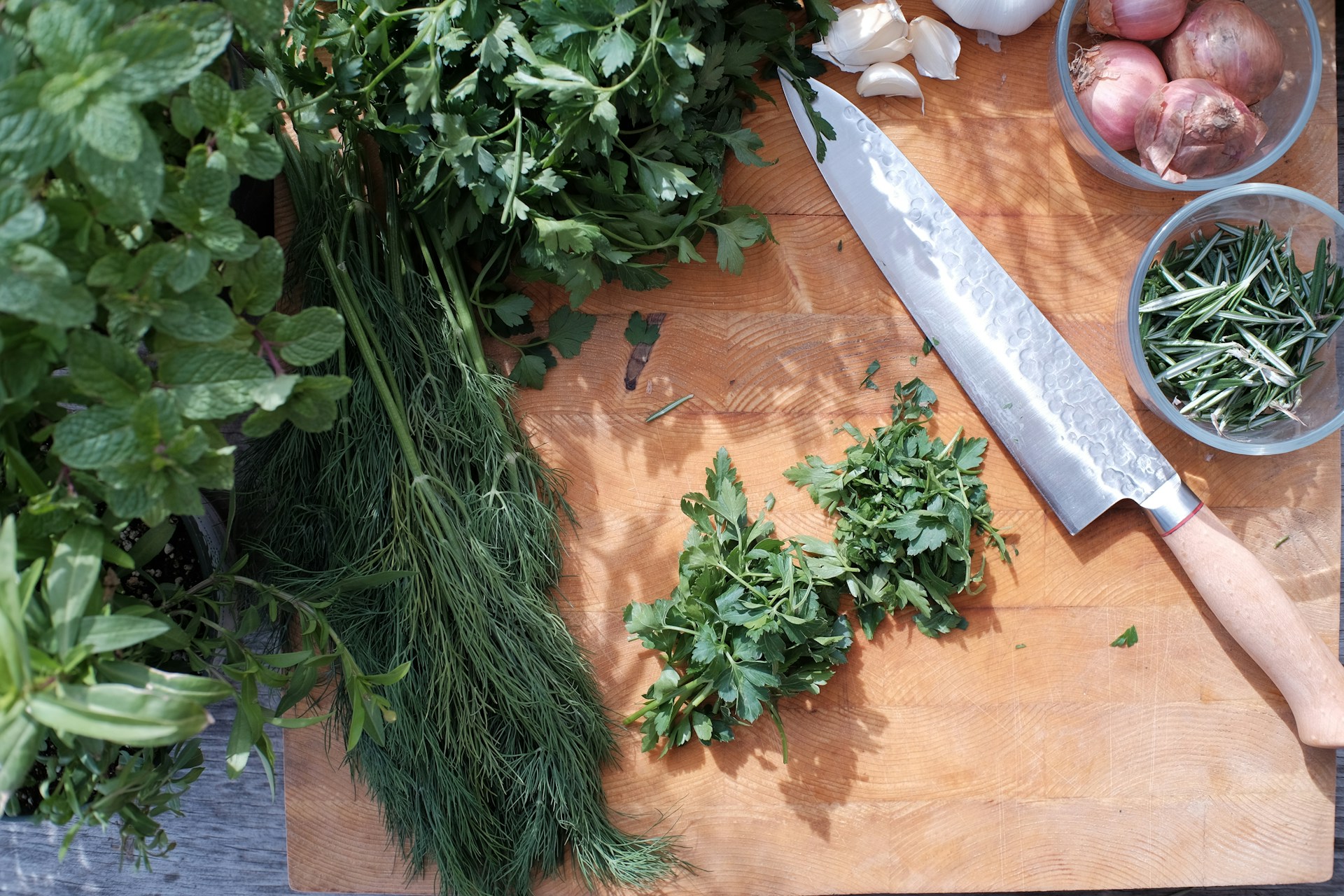 Fresh herbs on a wooden cutting board next to a chef's knife.